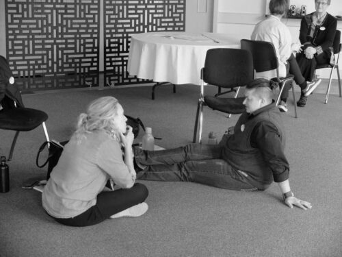 Photo showing two people sitting on the ground chatting at tht ePalmerston North Codesign Summit